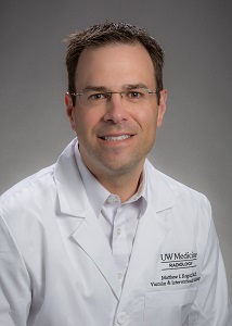 A headshot of Dr. Matthew Kogut. Dr. Kogut wears a white lab coat that reads "UW Medicine" over a white button-up shirt. Dr. Kogut wears glasses, has brown hair, and smiles gently into the camera.
