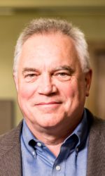 A photo of Dr. Paul Kinahan. In the photo, Paul wears a blue button-up shirt, beige blazer, and he smiles into the camera.