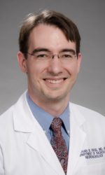 A photo of Dr. Nathan Cross. In the photo, Dr. Cross smiles at the camera. He wears glasses, a white lab coat, and a button-up shirt and tie.