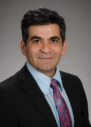 A photo of Dushyant Sahani. Dr. Sahani wears a dark suit, collared shirt, and tie. He looks confidently into the camera.