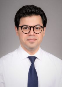 A portrait of Dr. Majid Chalian, who is wearing black rimmed glasses, a white button up shirt and navy blue tie.