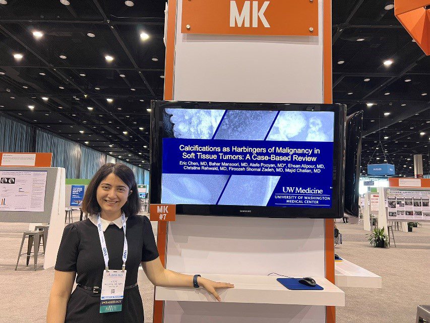 Atefe Pooyan, MD, MPH, poses in front of her presentation slide at RSNA. She stands in a large room, smiling and wearing professional attire.