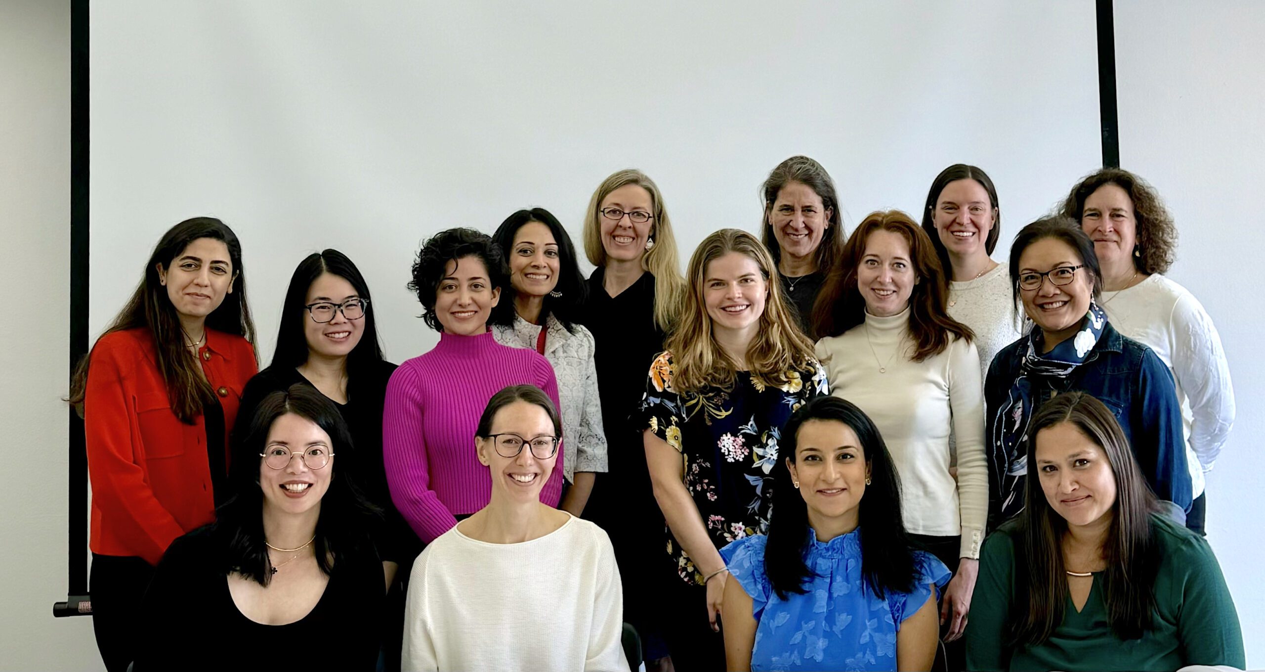 Fifteen members of the Women in Radiology club poses for a group photo. They wear business casual attire and are smiling.