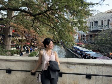 Dr. Khoshpouri stands on a bridge over a body of water with trees and buildings behind her.